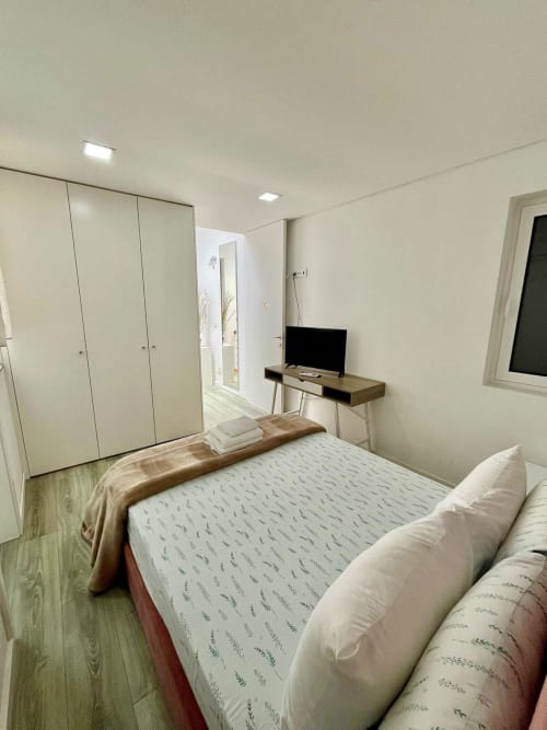 Modern bedroom at Casa Augusta hostel in Braga, Portugal with queen bed, wardrobe, TV desk, and air conditioning