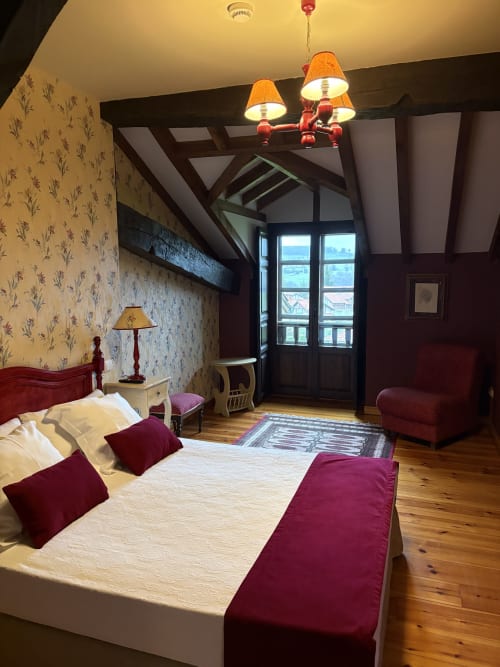 Amplia habitación doble en Hotel Palacio La Casona de Cerrazo con detalles en burdeos, techos con vigas y vistas al jardín