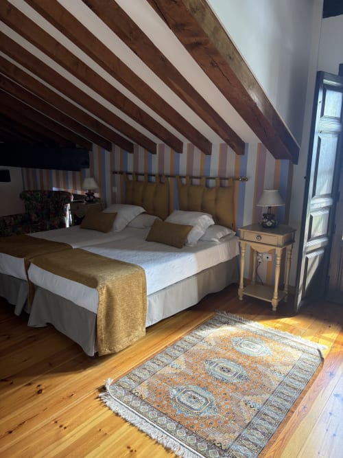 Elegante dormitorio abuhardillado en Hotel Palacio La Casona de Cerrazo con vigas de madera vista, paredes a rayas y decoración tradicional