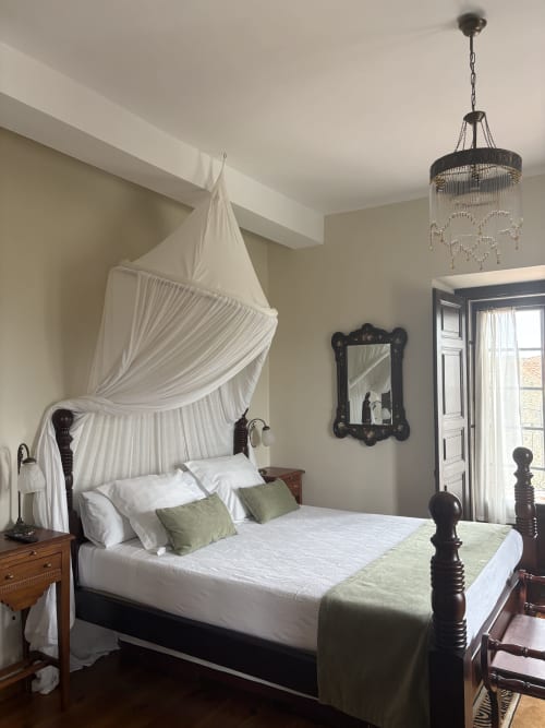 Elegante cama con dosel y cortinas blancas en la suite del Hotel Palacio La Casona de Cerrazo, con muebles de madera oscura y vistas a la montaña