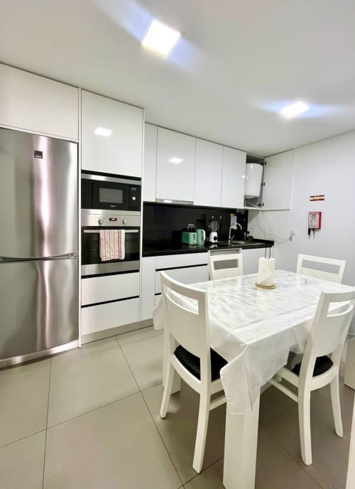 Modern kitchen and dining area at Casa Augusta hostel in Braga, Portugal with white cabinetry, black countertops, stainless