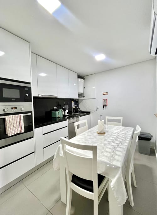 Modern kitchen and dining area in Suite C at Casa Augusta hostel, Braga, featuring white cabinets, black countertops, and