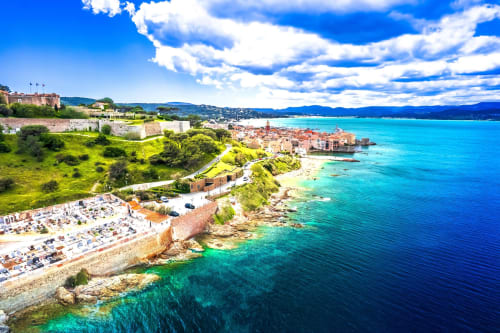 Eaux turquoise de la Méditerranée et falaises côtières à l'hôtel Cavalaire-sur-Mer avec ville historique et montagnes.