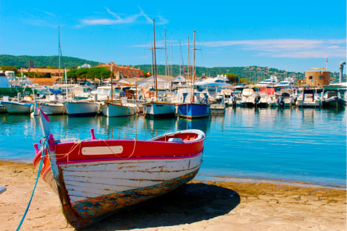 Bateaux de pêche rouge et bleu amarrés sur la plage de sable à Cavalaire-sur-Mer, France avec port méditerranéen et voiliers.