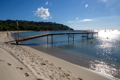 Plage ensoleillée de l'hôtel La Joya à Cavalaire-sur-Mer avec ponton en bois, eaux cristallines et littoral boisé