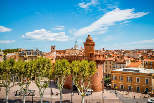 Pueblo medieval francés con tejados rojos, torre fortificada y plaza arbolada en Canet-en-Roussillon