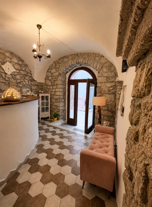Elegante ingresso ad arco in pietra presso Regnos Altos Boutique Rooms a Bosa, con sedute in terracotta e mattonelle esagonali