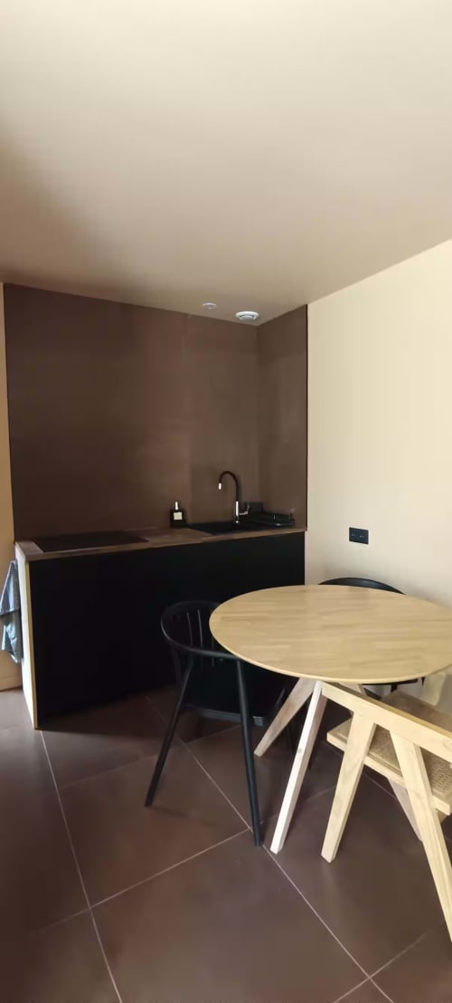 Kitchenette moderne avec mobilier sombre et table de salle à manger ronde en bois à la Garçonnière, Domaine Alga
