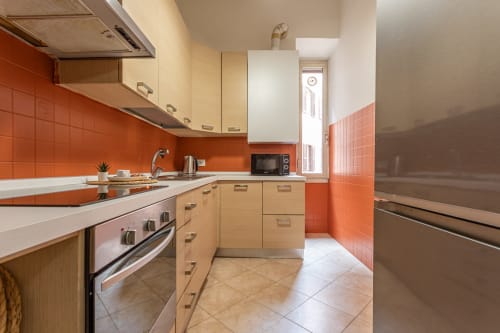 Cucina moderna nell'appartamento Terrestre Roma, Roma, con rivestimento in piastrelle arancioni, mobili in legno e acciaio inossidabile