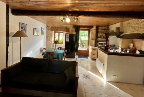 Espace de vie ouvert au Gîte La Vieille Ferme avec canapé noir, table à manger et cuisine équipée aux poutres en bois