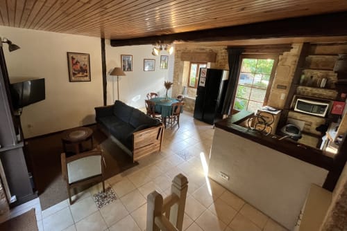Spacieux séjour ouvert à La Vieille Maison avec poutres apparentes, cheminée, table à manger, canapé noir et jardin