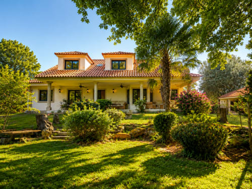 Casa de estilo español amarilla con techo de barro, columnas blancas y palmera en jardín exuberante junto al río Tomiño