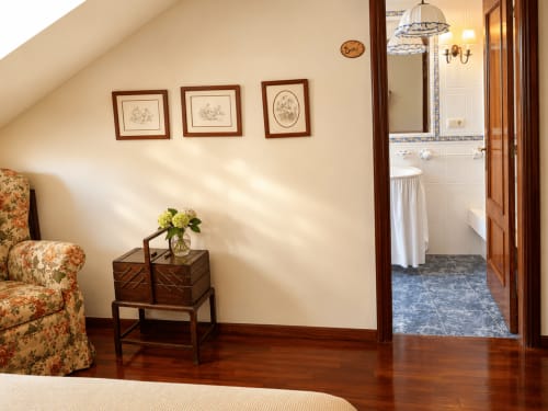 Elegante suite de dormitorio en cabaña Tomiño con muebles de madera, silla floral y baño privado con bañera y ducha