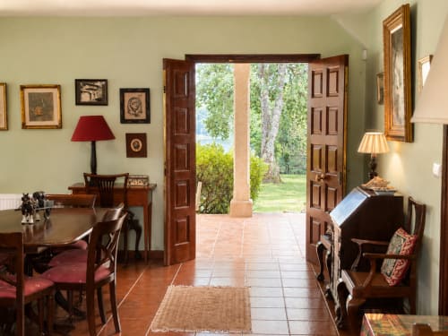 Interior elegante de cabaña en Tomiño con puertas abiertas al jardín fluvial, muebles de madera y paredes verdes