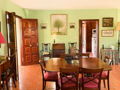 Comedor espacioso de la casa rural As Landras en Tomiño, con mesa de madera, sillas y paredes verde lima decoradas con paisajes