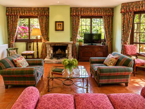 Elegante sala de estar en la casita As Landras, Tomiño, con sillones de cuadros, chimenea y vistas al río a través de grandes ventanales.