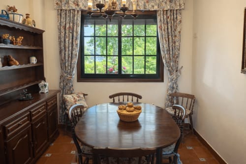 Elegante comedor con mesa redonda de madera, sillas y cesta de pan, con vistas a un río verde a través de ventanales con marco negro