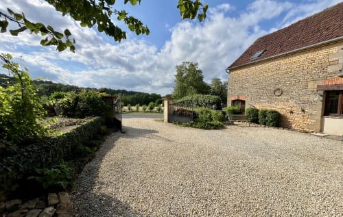 Cour en gravier du Gîte La Vieille Ferme de La Doinie à Saint-Geniès, avec bâtisse en pierre, jardins et vue sur la campagne