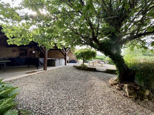 Cour ombragée avec graviers au Gîte La Vieille Ferme de La Doinie, bâtiments en pierre, zones de détente et belle canopée d'arbres