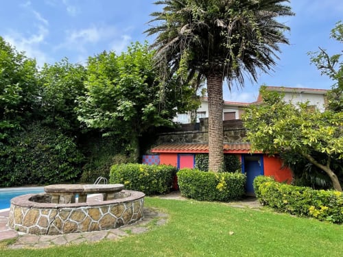 Patio de Casa Señorial Sasueta con hoguera de piedra, palmera, piscina y edificio rojo en San Sebastián