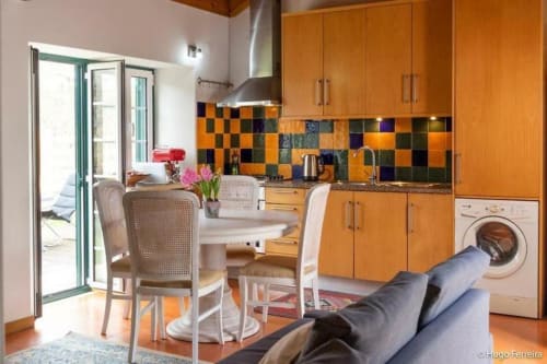 Modern kitchen-dining area at Quinta Boa Vida villa in Alcobaça with orange cabinetry, colorful tile backsplash, and garden