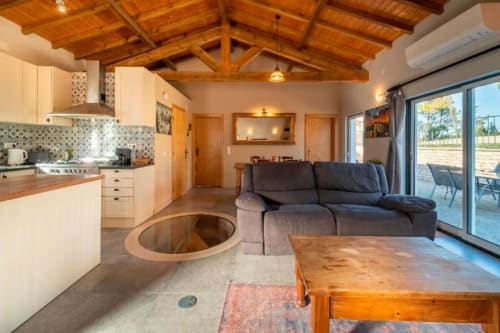 Open-plan living area with kitchen, fireplace, gray sofa and wooden beams at Quinta Boa Vida villa in Alcobaça, Portugal