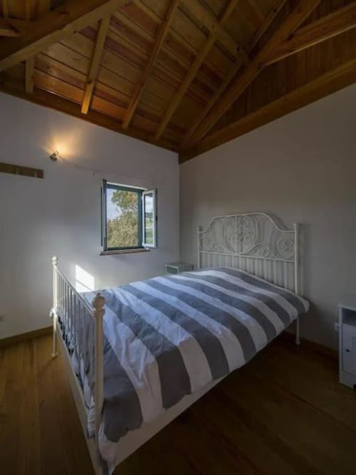 Bright bedroom with white metal bed, striped bedding, exposed wooden ceiling beams, and garden views at Quinta Boa Vida in