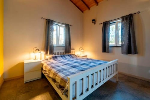 Bright bedroom at Quinta Boa Vida in Alcobaça with white bed, bedside lamps, two windows with curtains, wooden ceiling beams,