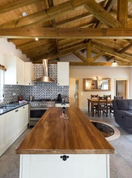 Modern open-plan kitchen and dining area with wooden beam ceiling, white cabinetry, patterned backtile, and wooden island at