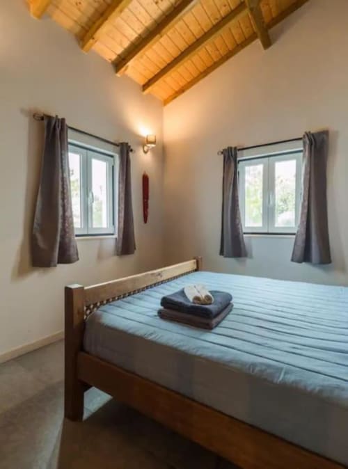 Bright bedroom in Quinta Boa Vida villa with wooden ceiling beams, blue bedding, and garden views through two windows with