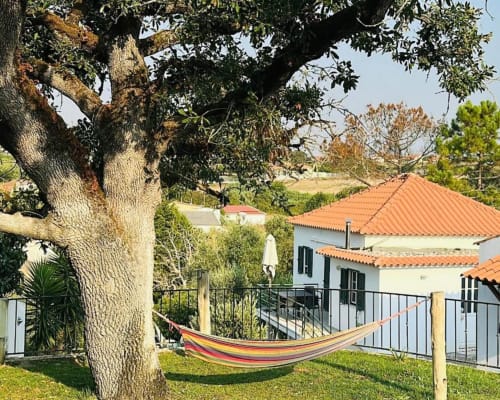 Colorful hammock strung between trees in the garden at Quinta Boa Vida, Alcobaça, with white villa and terracotta roof