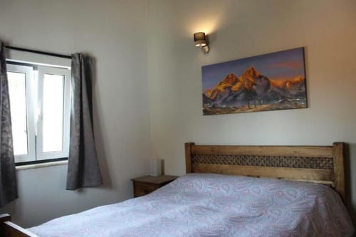 Cozy master bedroom at Quinta Boa Vida in Alcobaça with wooden bed, mountain landscape artwork, window with garden view, and