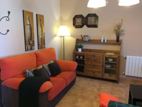 Luminoso salón de La Senda del Duratón con sofá naranja, muebles de madera e iluminación cálida en Sebúlcor