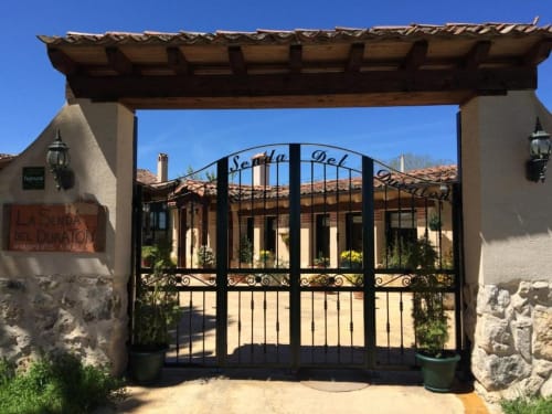 Ornamentada puerta de hierro forjado negro en la entrada del hotel La Senda del Duraton en Sebúlcor con arquitectura rústica española