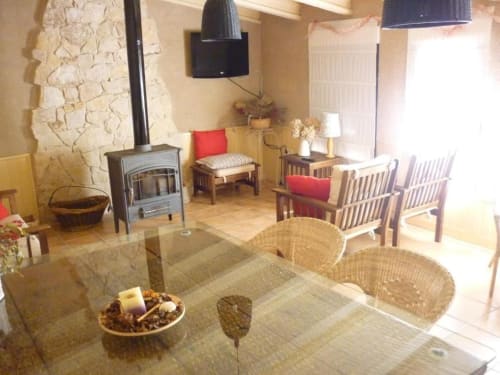Acogedora sala de estar en La Senda del Duraton con chimenea, muebles de madera, cojines rojos e iluminación natural