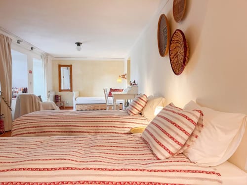 Quarto luminoso na Quinta da Mata de Baixo com cama de listras vermelhas e creme, cestos decorativos na parede e vista para o jardim
