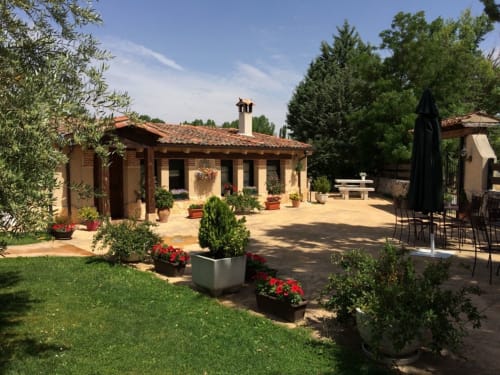 Patio de La Senda del Duraton con villa de terracota, jardines cuidados, macetas florales y zona de comedor en Sebúlcor
