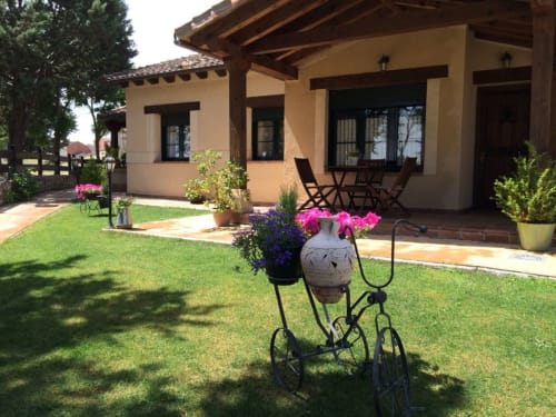 Patio de La Senda del Duraton con acogedora casa de estilo ranch, jardín bien cuidado, maceta decorativa con bicicleta y flores rosas