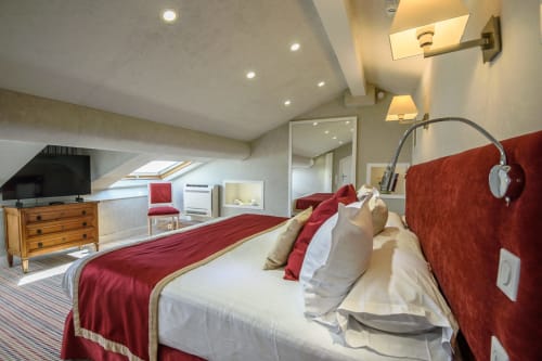 Suite mansardata di lusso all'Hotel Splendid Cannes con testata imbottita rossa, biancheria bianca, cassettone in legno, TV e atmosfera