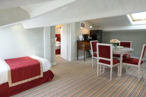 Spaziosa suite mansardata all'Hotel Splendid Cannes con biancheria rossa e bianca, zona pranzo e lucernario