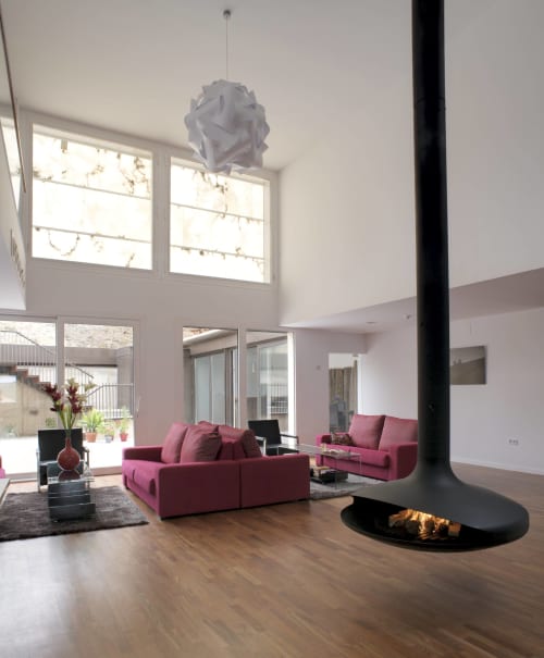 Sala de estar moderna en Hostal Doña Blanca con sofás rosas, chimenea central, lámpara colgante y techos altos