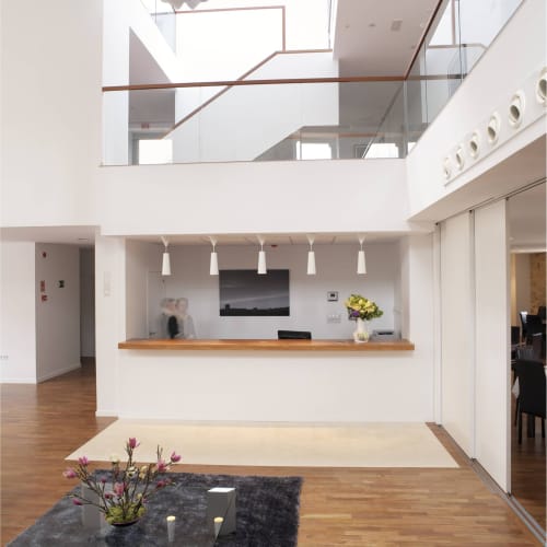 Moderno vestíbulo del Hostal Doña Blanca con paredes blancas, mostrador de madera, luces colgantes y atrio de doble altura