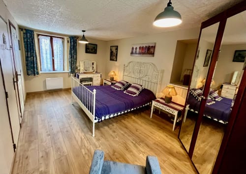 Chambre spacieuse du Gîte La Vieille Ferme de La Dounie à Saint-Geniès avec lit en métal blanc, literie violette et vue sur le jardin.