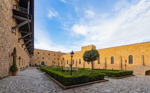 Patio medieval del Hostal Doña Blanca en Sigüenza con muros de piedra, jardines cuidados y arquitectura histórica