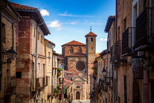 Edificios medievales de piedra bordean una calle estrecha en Sigüenza, España, con una iglesia histórica que cuenta con un campanario
