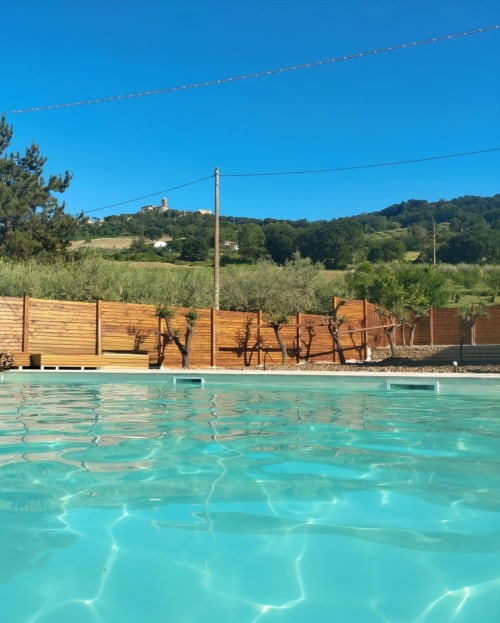 Piscina turchese dell'hotel Queen a Campofilone, Italia con bungalow in legno e ulivi nella campagna ondulata