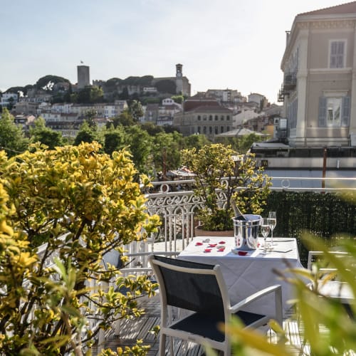 Elegante terrazza per cena all'Hotel Splendid Cannes con vista sulla città e sul lungomare, circondata da lussureggianti piante