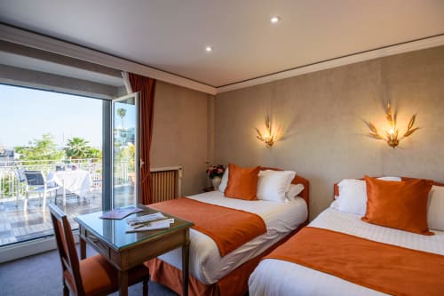 Camera di lusso all'Hotel Splendid Cannes con letti gemelli, accenti arancioni e terrazza privata con vista sulla città
