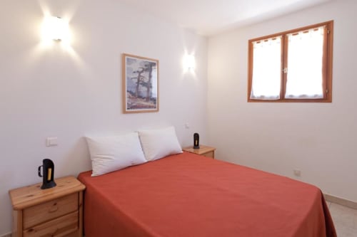Chambre lumineuse à la villa Casa Callista Est avec literie rouge, oreillers blancs, tables de nuit en bois et vue sur le jardin