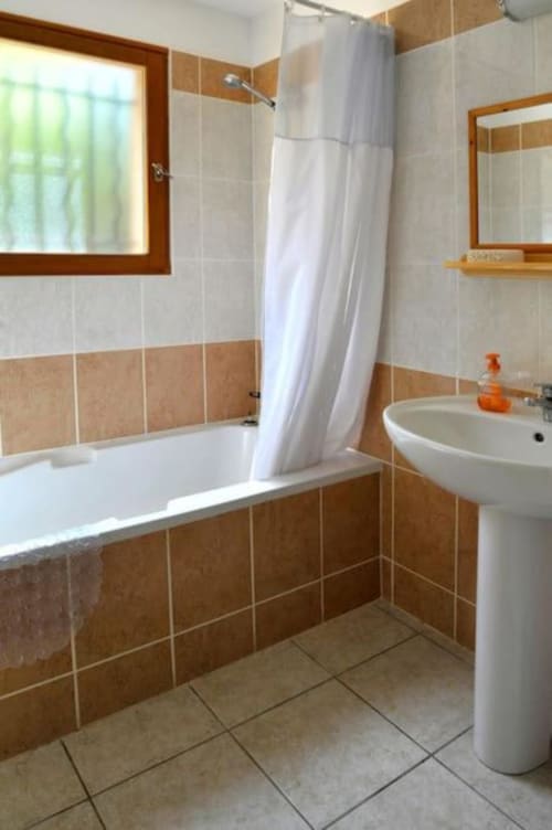 Salle de bain moderne de la villa Casa Callista Est avec carrelage marron et beige, lavabo blanc sur piédestal, baignoire avec rideau de douche